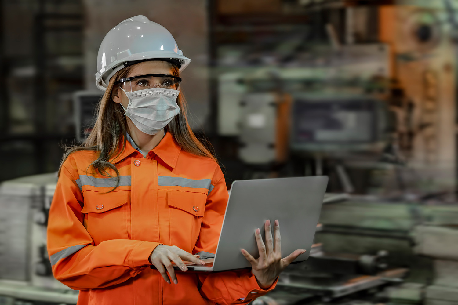 Female engineer wearing hard hat and facemask holding laptop at waste plant