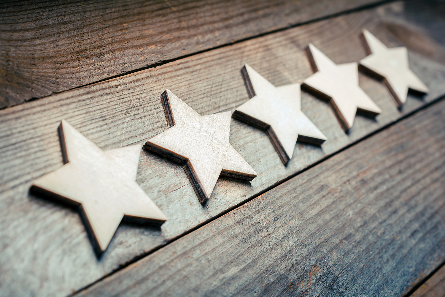 Five wooden stars lined up on a wooden board with heavy depth of field bluring the furthest stars.